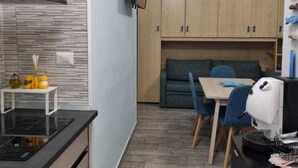 Una cocina compacta con encimera negra, armarios de madera y un pequeño comedor con mesa y sillas.