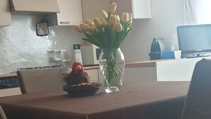 A dining area with a table set for two, a vase with flowers, and a stuffed toy on the table.