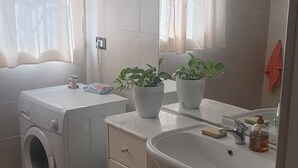 A compact bathroom with a washing machine, a sink, and two potted plants.