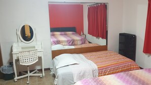 A bedroom with two beds, a desk with a chair, a radiator, and a mirror.