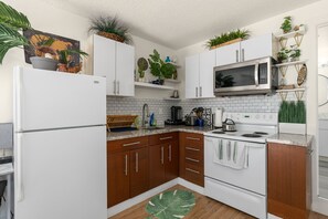A modern kitchen with white cabinets, a microwave, an oven, and a sink. There are plants on the shelves and a large green leaf rug on the floor. - New Jungle Vibes Theme, Your own unit B  (Edgewood)
