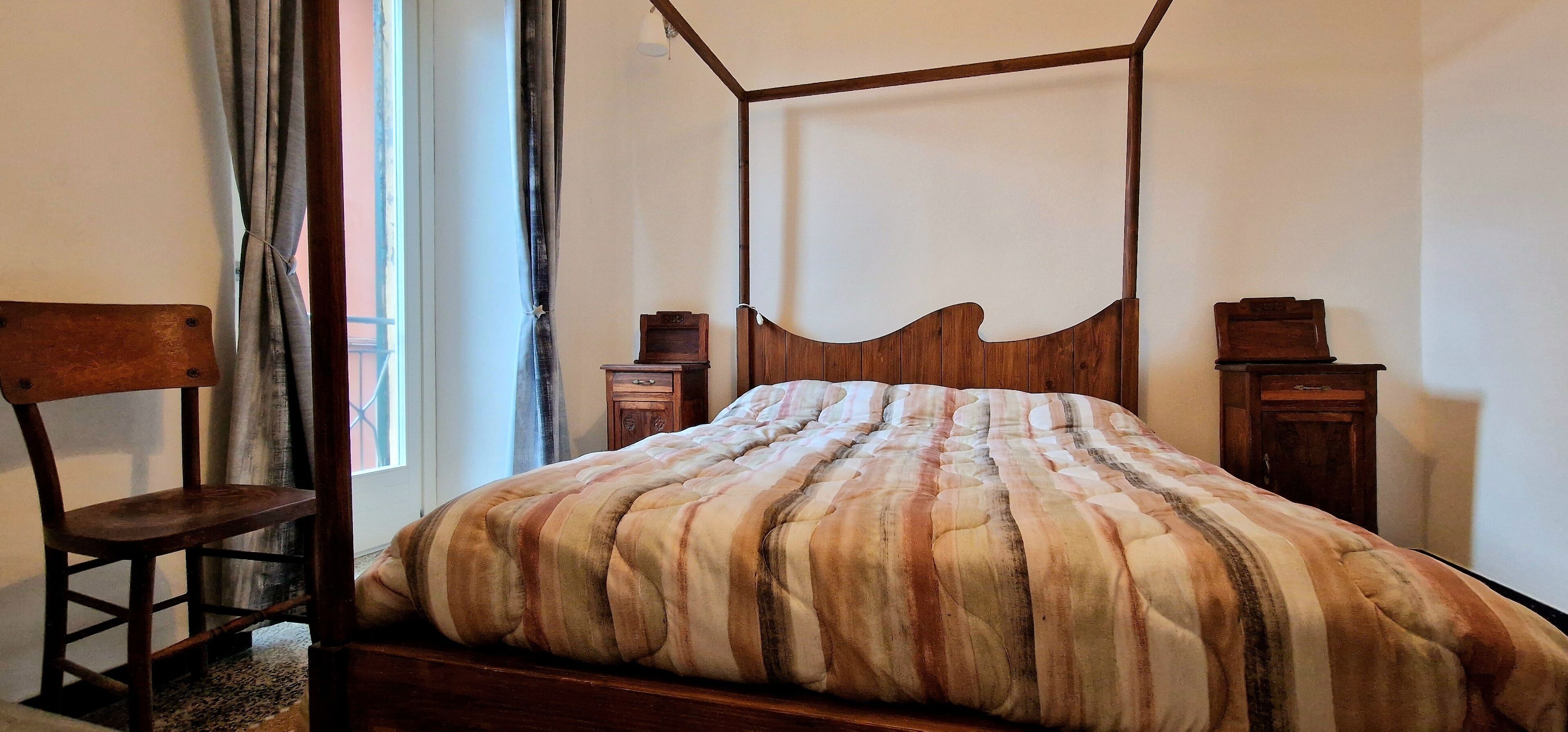 Un letto a baldacchino con copripiumino a righe, una sedia di legno e un comodino con una sveglia.