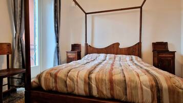 Un letto a baldacchino con copripiumino a righe, una sedia di legno e un comodino con una sveglia.