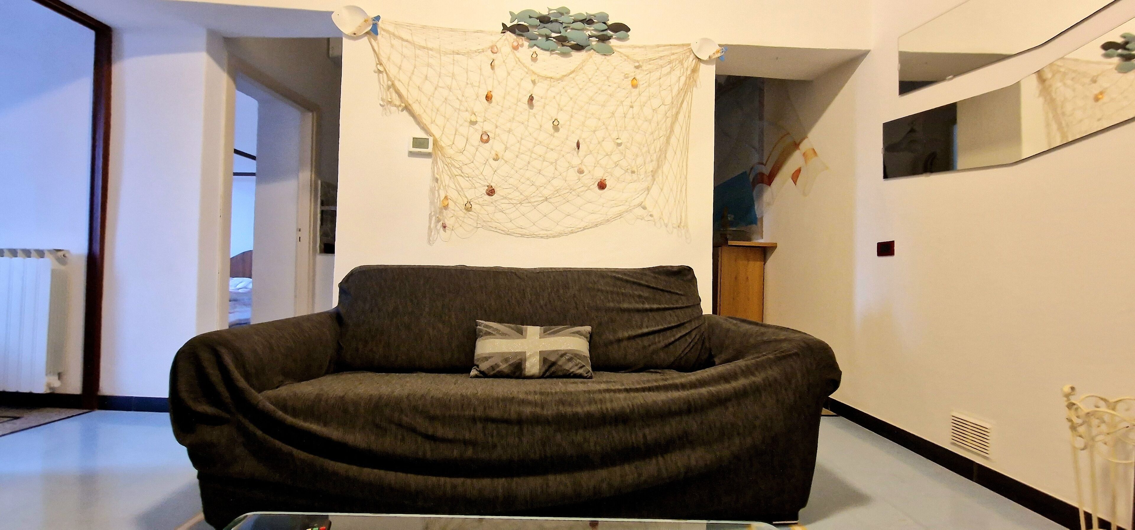 A modern living room with a dark brown sofa, a cushion with a flag design, and a decorative net with stones on the wall.