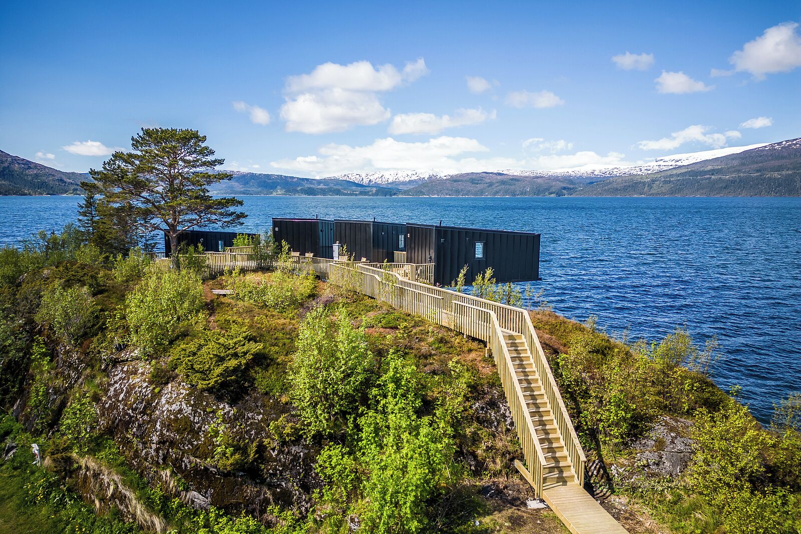 A waterfront property with a wooden staircase leading to a dock, surrounded by lush greenery and a clear blue lake.