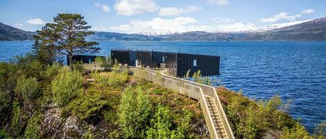 Una propiedad frente al lago, con una escalera de madera que conduce a un muelle, rodeada de exuberante vegetación y un lago azul cristalino.