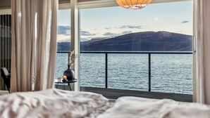 A bedroom with a large window overlooking a lake and mountains.