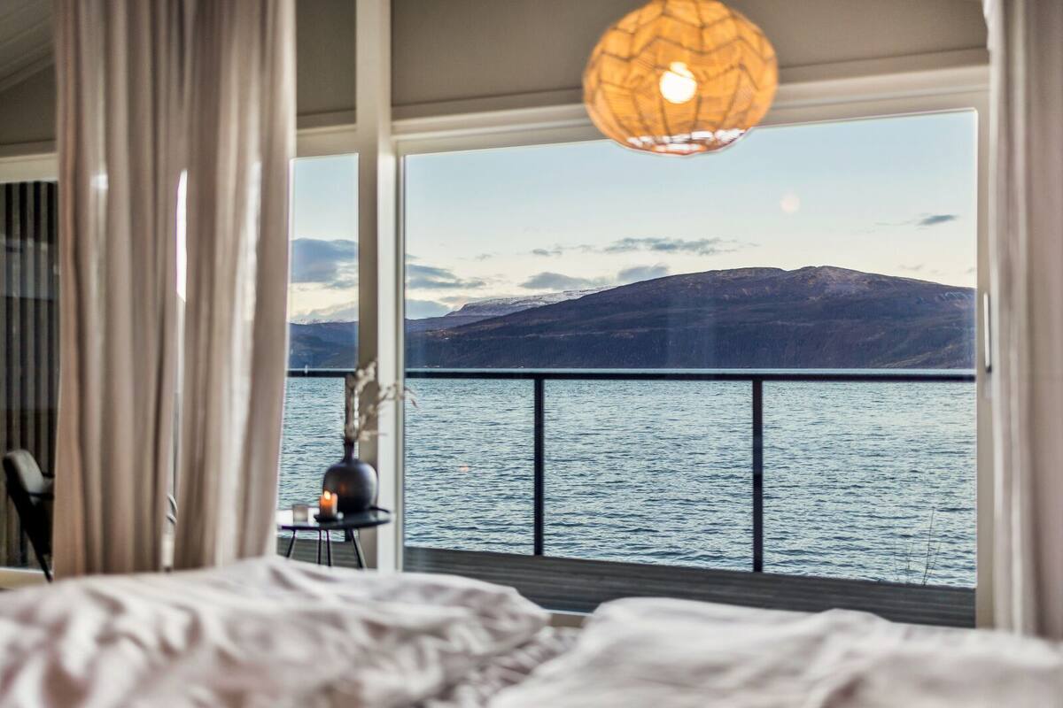 A bedroom with a large window overlooking a lake and mountains.