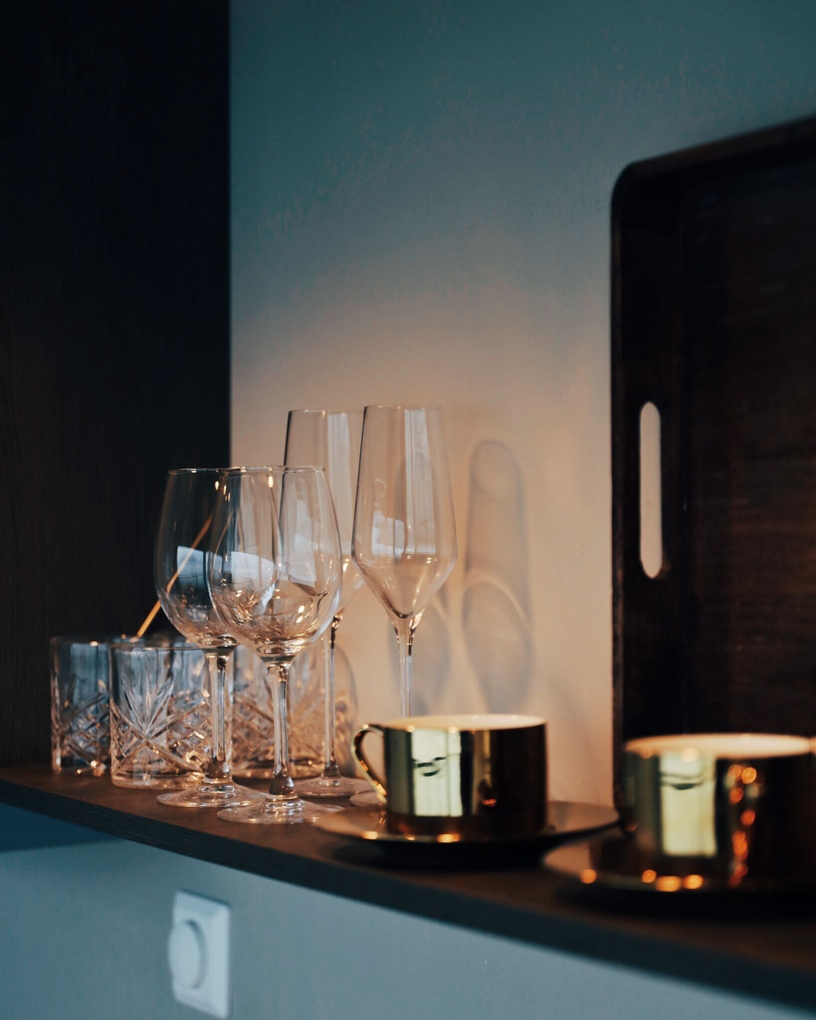A shelf with various glassware, including wine glasses and a gold-colored mug, against a dark background.