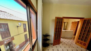 A room with a bed, a window with a view of a building labeled "Vilaflor Hotel Rural," and a door leading to another room. - Alma Hostel (Vilaflor)