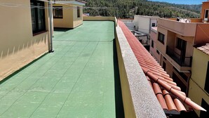 A rooftop terrace with a green floor, terracotta roof tiles, and a view of a forested hillside. - Alma Hostel (Vilaflor)