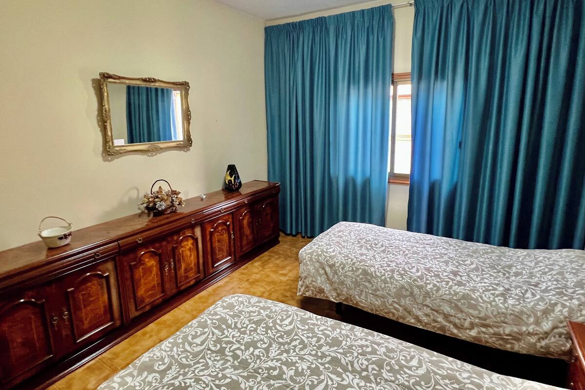 Une chambre avec deux lits, une commode en bois, un miroir et des rideaux bleus.