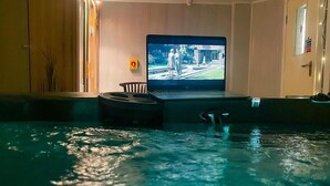A swimming pool with a television screen displaying a scene, surrounded by a wooden cabinet and a door. - The Chatwal Boutique Hotel (Blackpool)