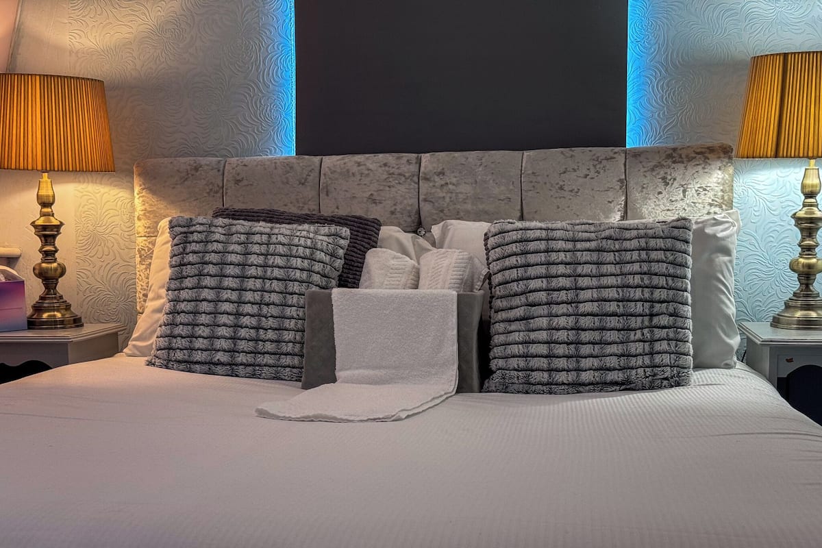 A neatly made bed with a grey headboard, multiple pillows, and two bedside lamps.