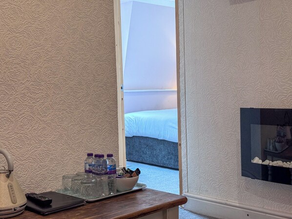 A hotel room with a wooden desk, a kettle, water bottles, a bowl, and a tray.