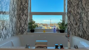 Ein Badezimmer mit großem Fenster, zwei Kübelpflanzen, einer Badewanne und einer Handstange.