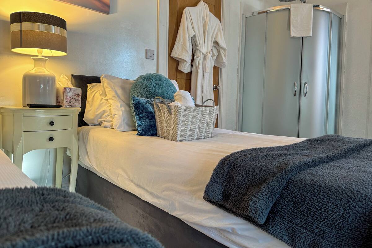 A neatly made bed with pillows, a bedside lamp, a basket, and a robe hanging on a door.