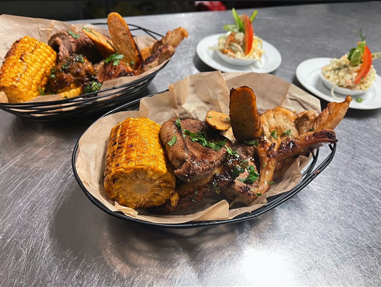 Una mesa de comedor con una cesta que contiene carne a la parrilla y mazorcas de maíz.