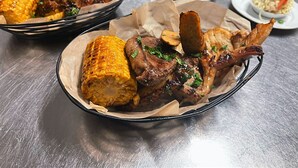 Ein Esstisch mit einem Korb, der gegrilltes Fleisch und Mais enthält.