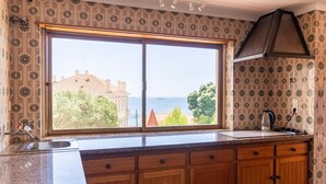 Una cocina con un ventanal grande, armarios de madera y vistas al mar y edificios.