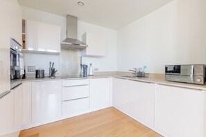 A modern kitchen with white cabinetry, a stainless steel range hood, a built-in oven, and a microwave. - Radiant 1BDR Retreat with WiFi in North Maida Vale (London)