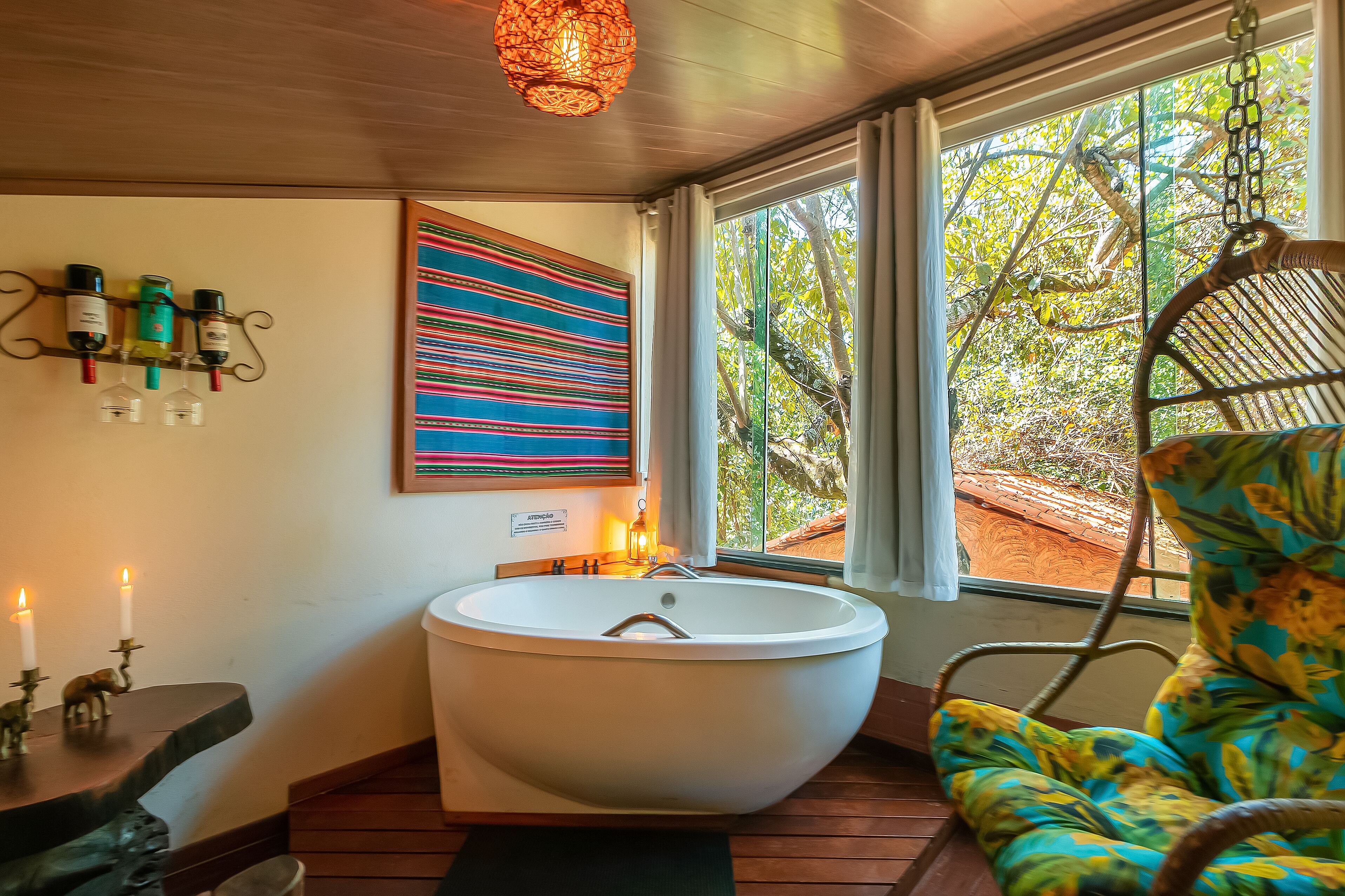 Ein Badezimmer mit freistehender Badewanne, einem Hängekorbsessel, einem Wandweinkeller und einem farbenfrohen abstrakten Gemälde.