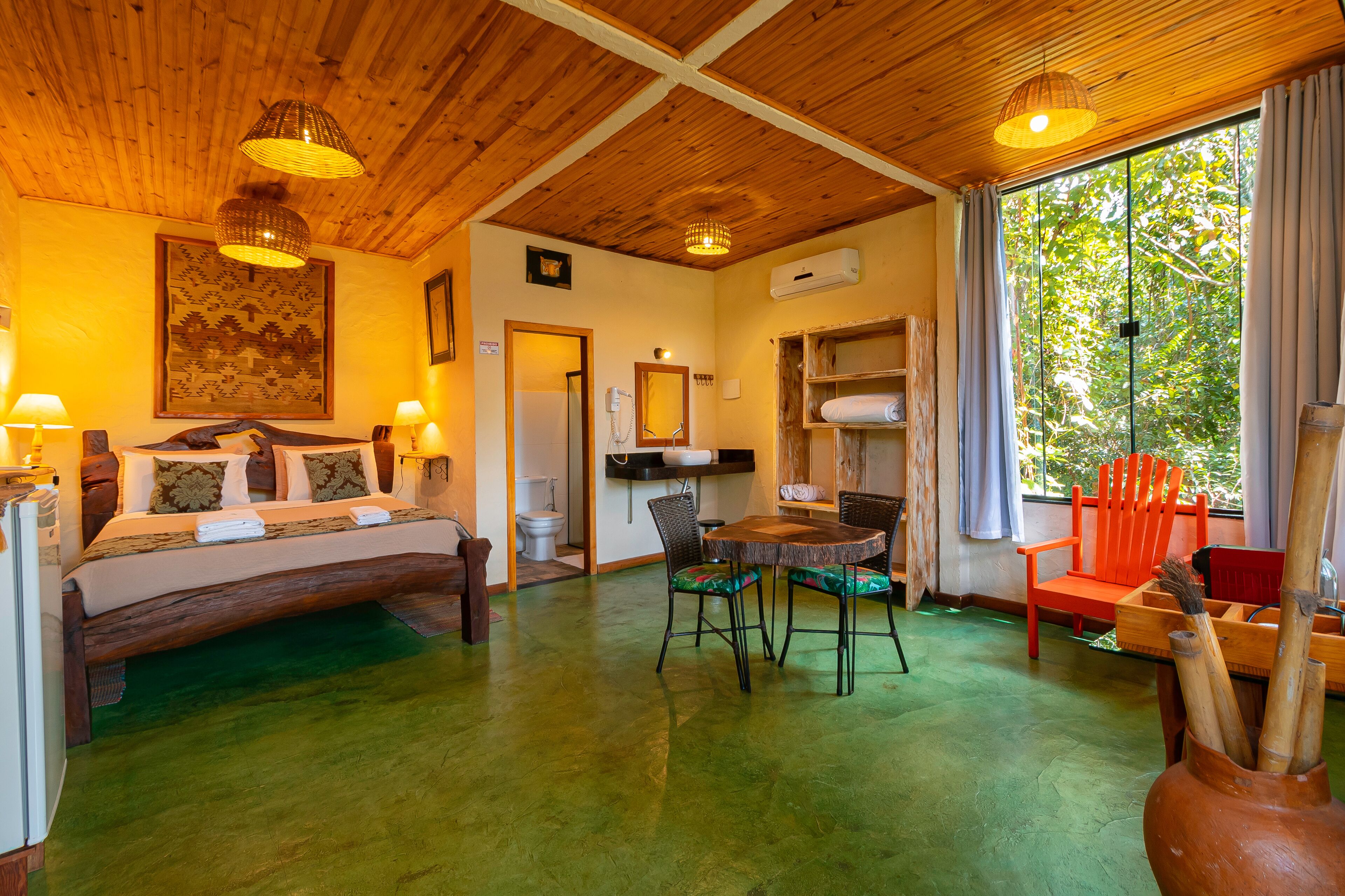 A room with a bed, a dining table, chairs, a wooden ceiling, and a window with curtains.