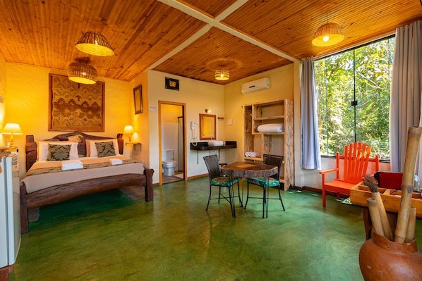 Una habitación con cama, una mesa de comedor, sillas, techo de madera y una ventana con cortinas.