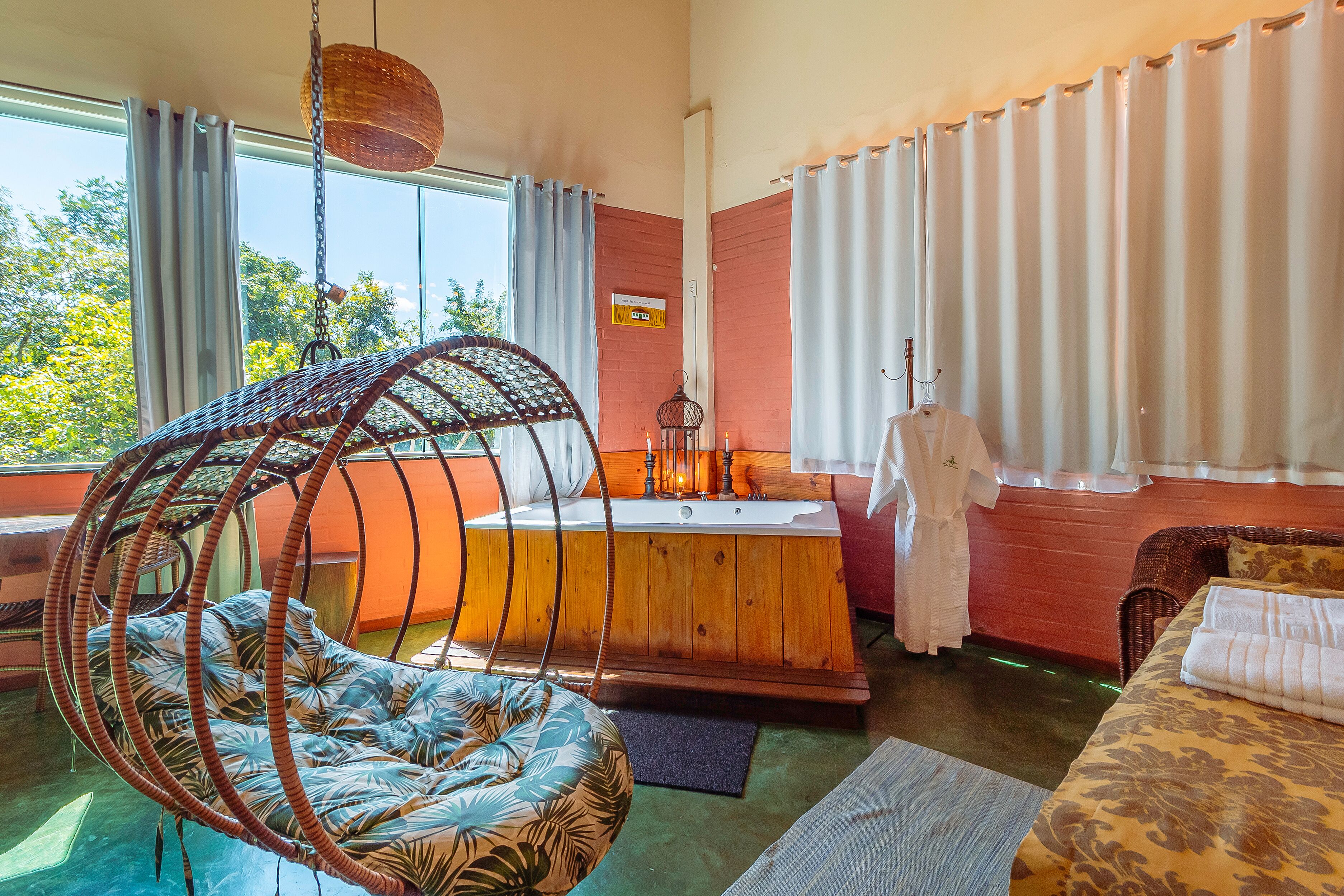 Una habitación con una silla colgante, una bañera y una cama con edredón estampado.