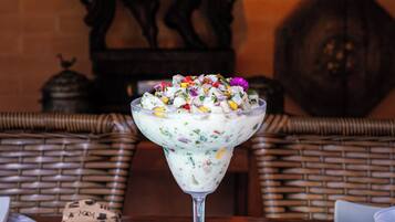 A dessert in a glass on a table with a wicker chair and a decorative wall in the background.