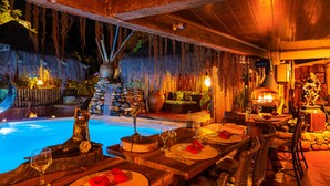 Een eetruimte met een zwembad, houten tafels, stoelen en een waterval.