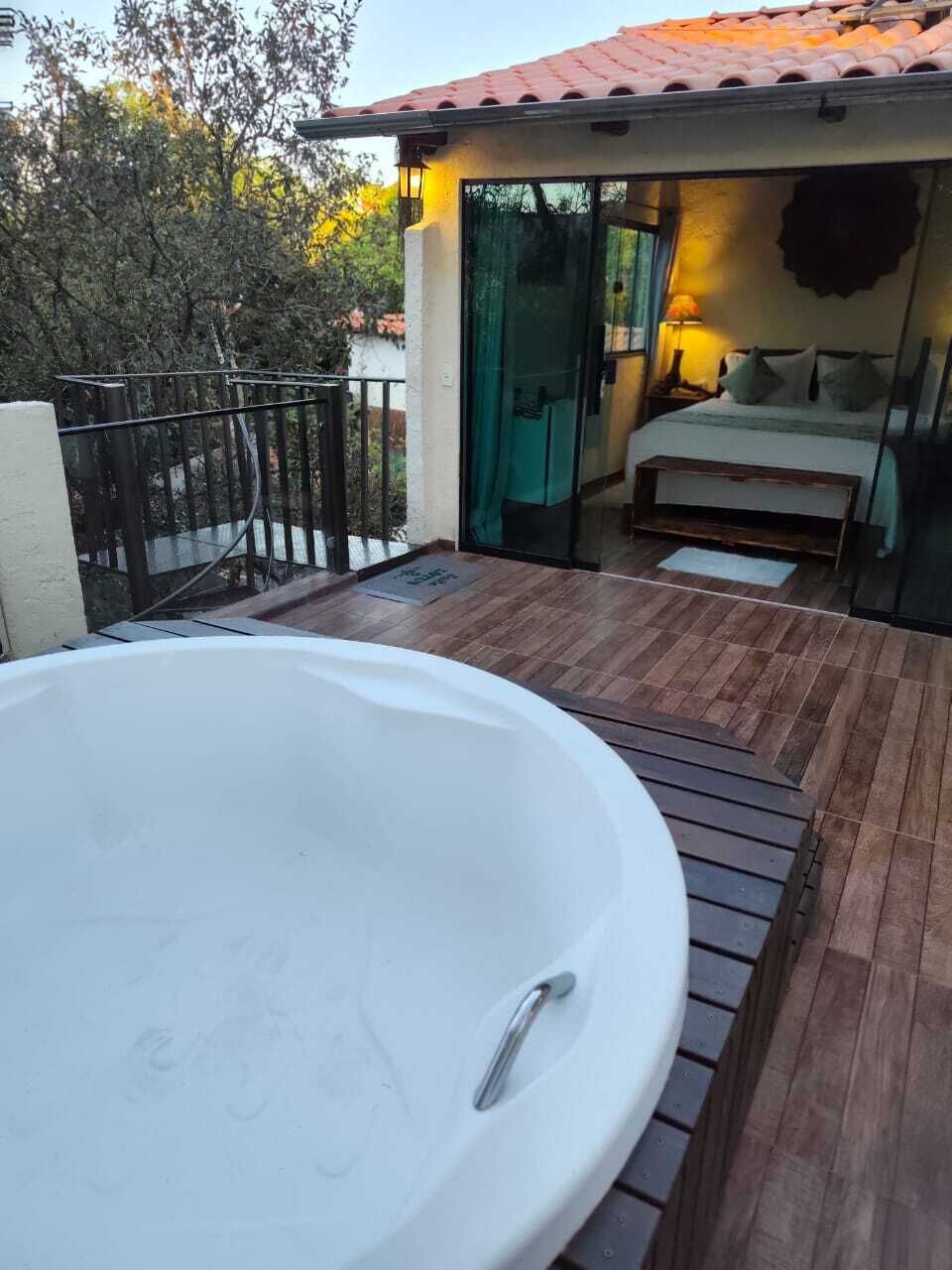 A hot tub on a wooden deck, a bedroom with a bed and a nightstand, and a glass door leading to the interior.