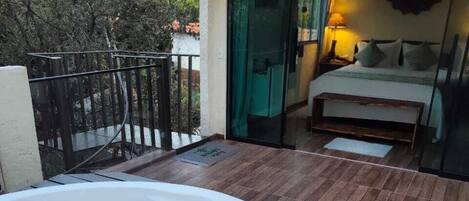 A hot tub on a wooden deck, a bedroom with a bed and a nightstand, and a glass door leading to the interior.