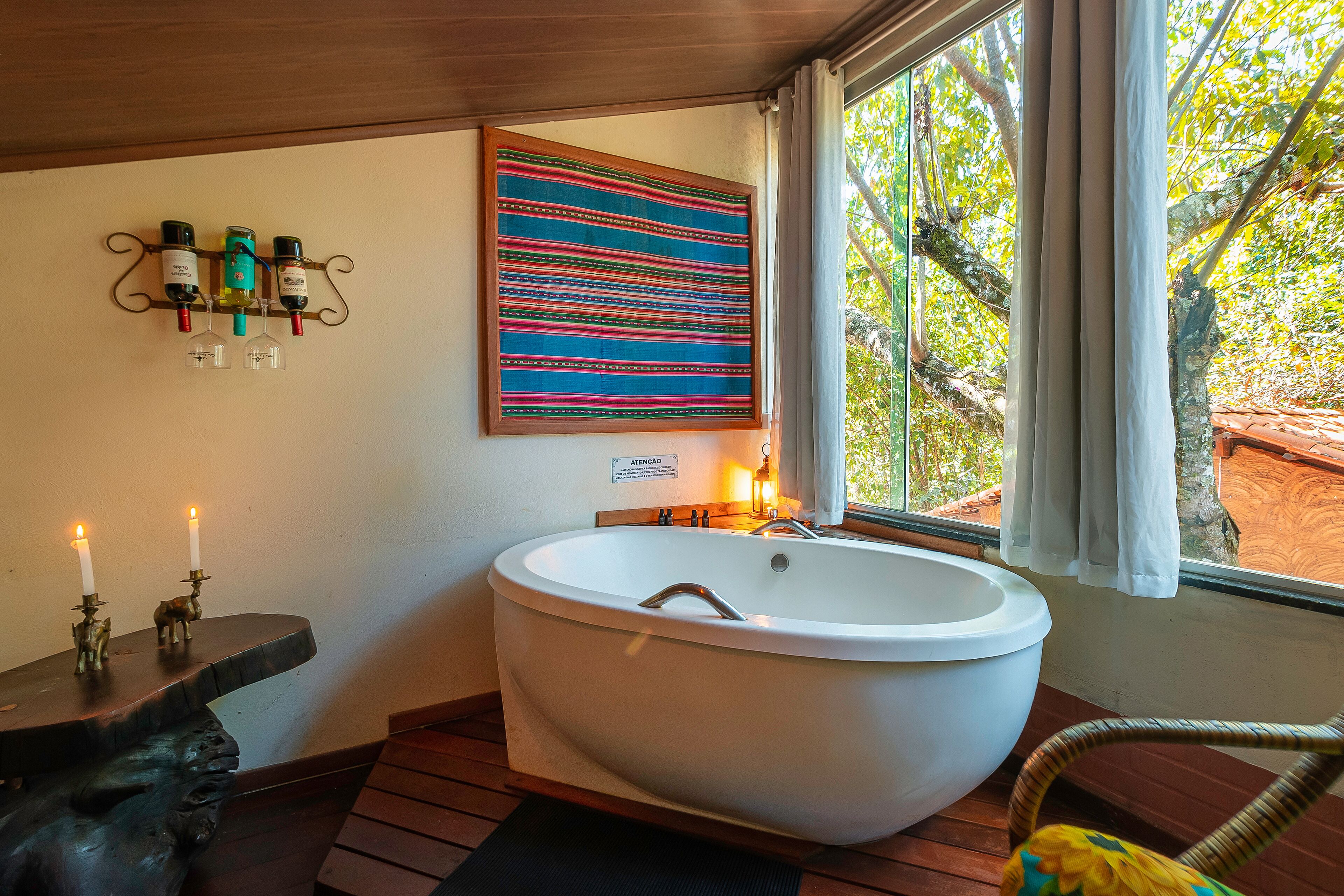 A bathroom with a freestanding bathtub, a wall-mounted wine rack, and a large window with a view of trees.