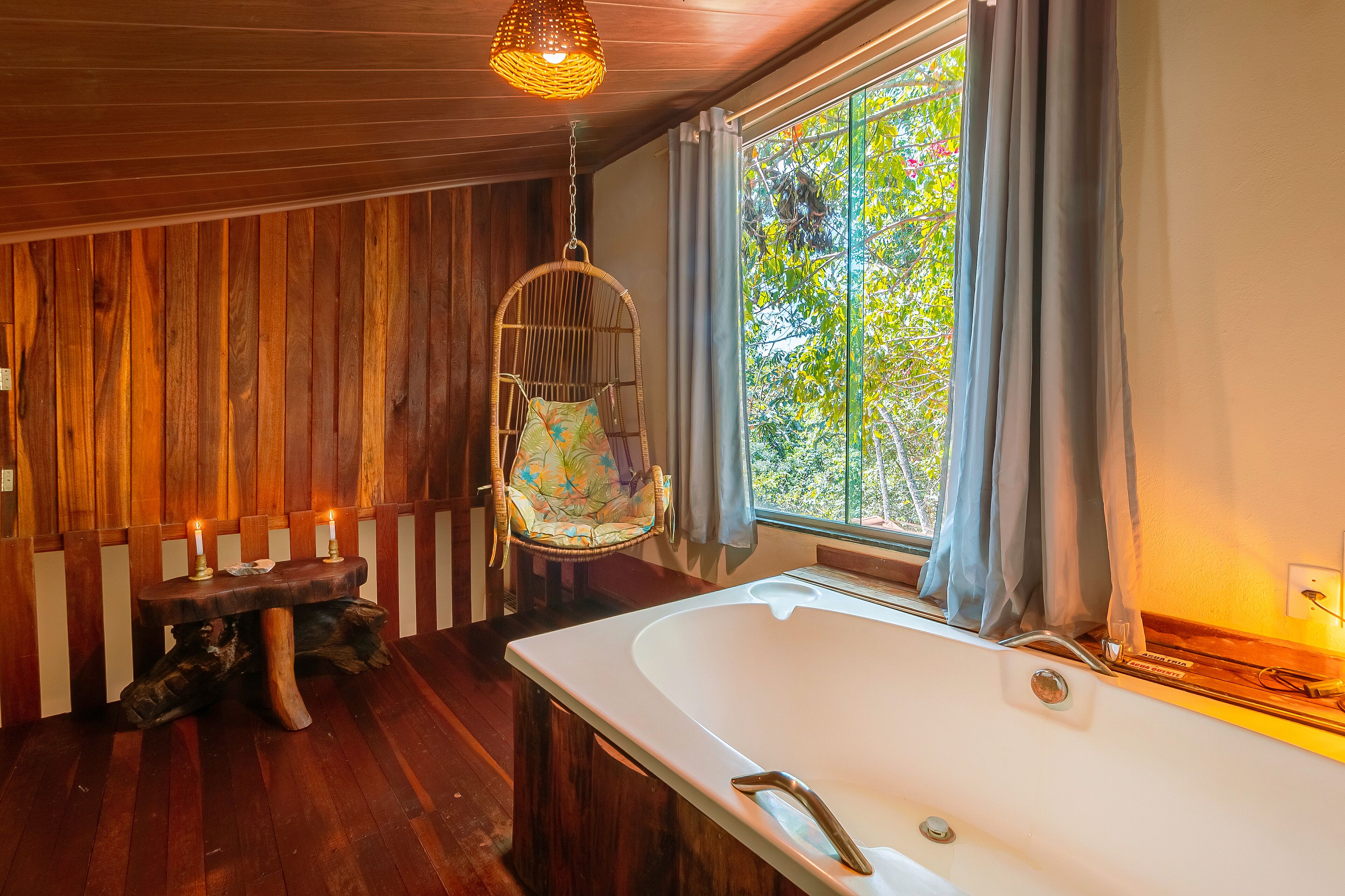 Una habitación de madera con una bañera grande, un sillón colgante y una mesa con velas.