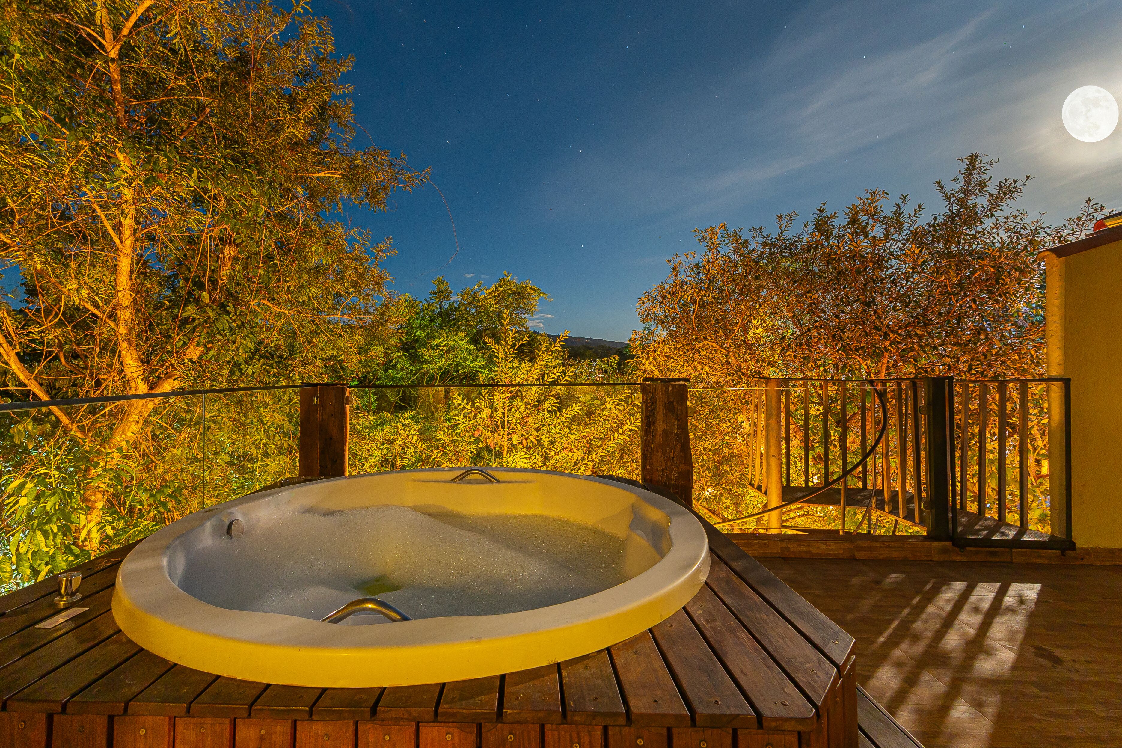 A hot tub on a wooden deck with a view of trees and a moon in the sky.