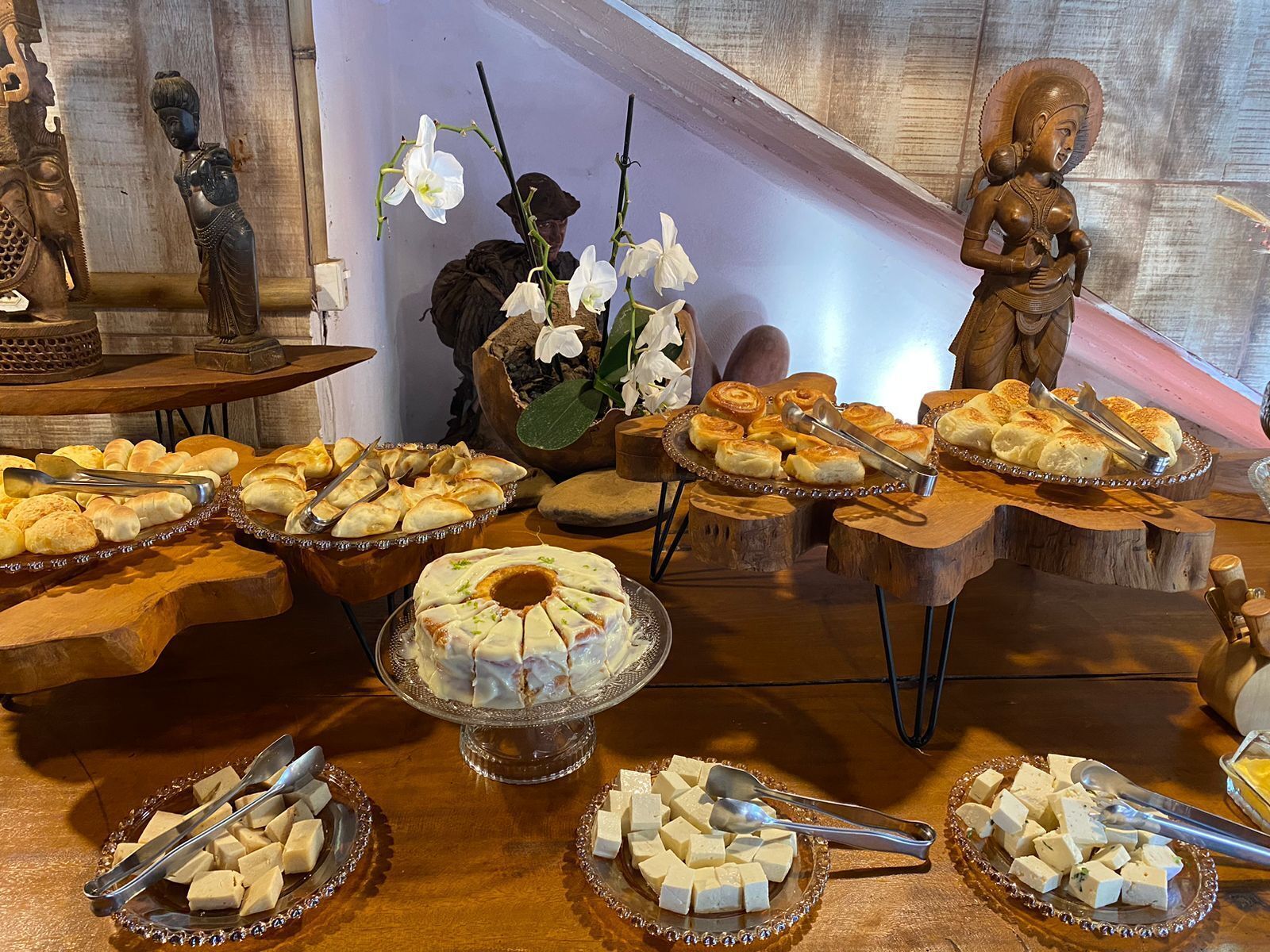 A buffet table with various food items, including pastries, bread, and cheese, arranged on wooden stands and glass dishes.