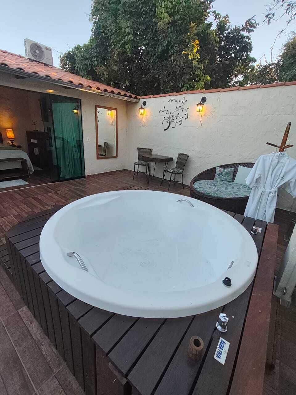 Un espace extérieur avec un jacuzzi, une terrasse en bois, une petite table, des chaises et un luminaire fixé au mur.