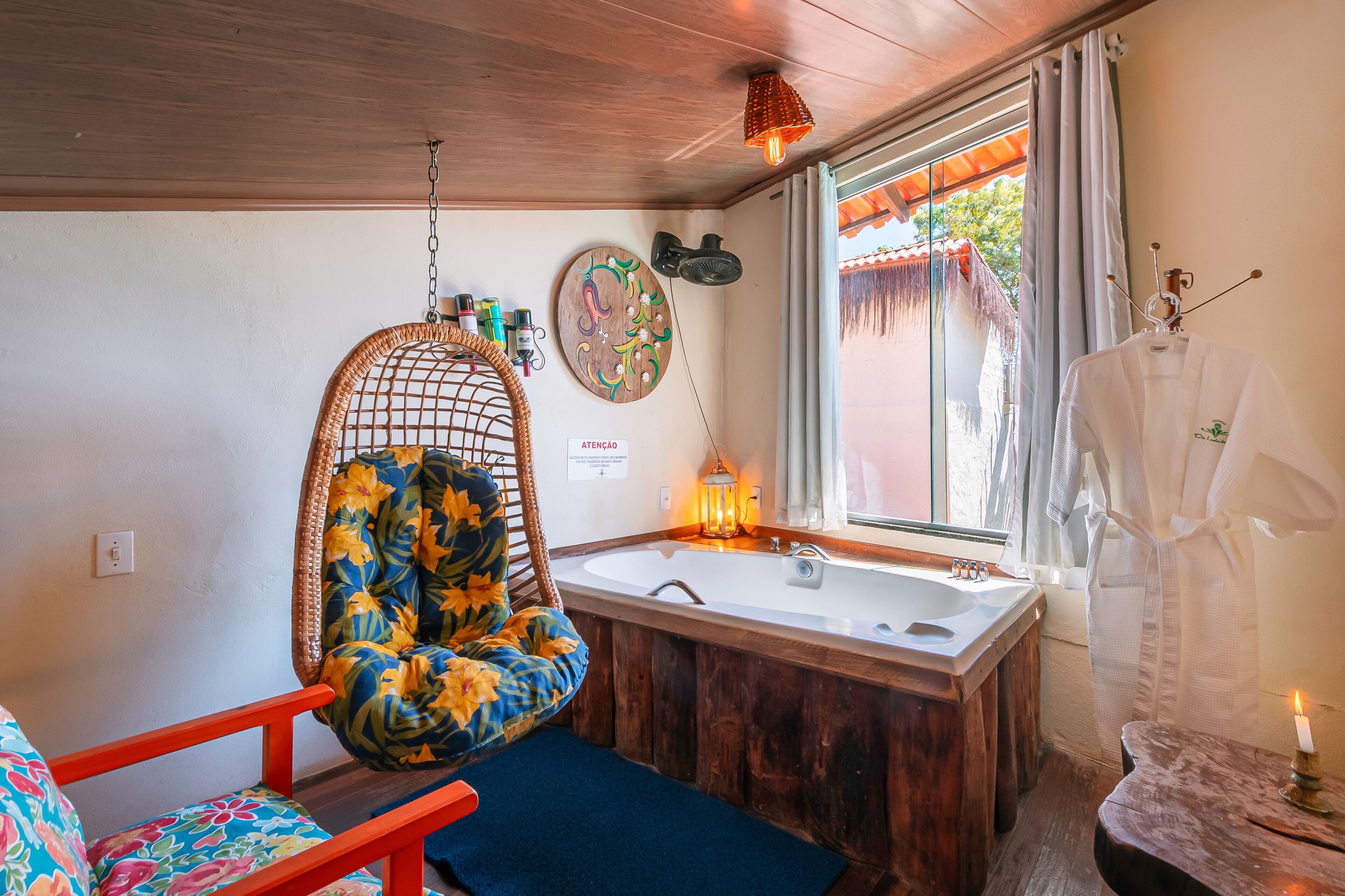 A bathroom with a wooden bathtub, a hanging chair, a sink, and a window with curtains.