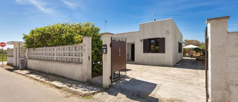 A modern building with a gated entrance, a concrete driveway, and a clear blue sky.
