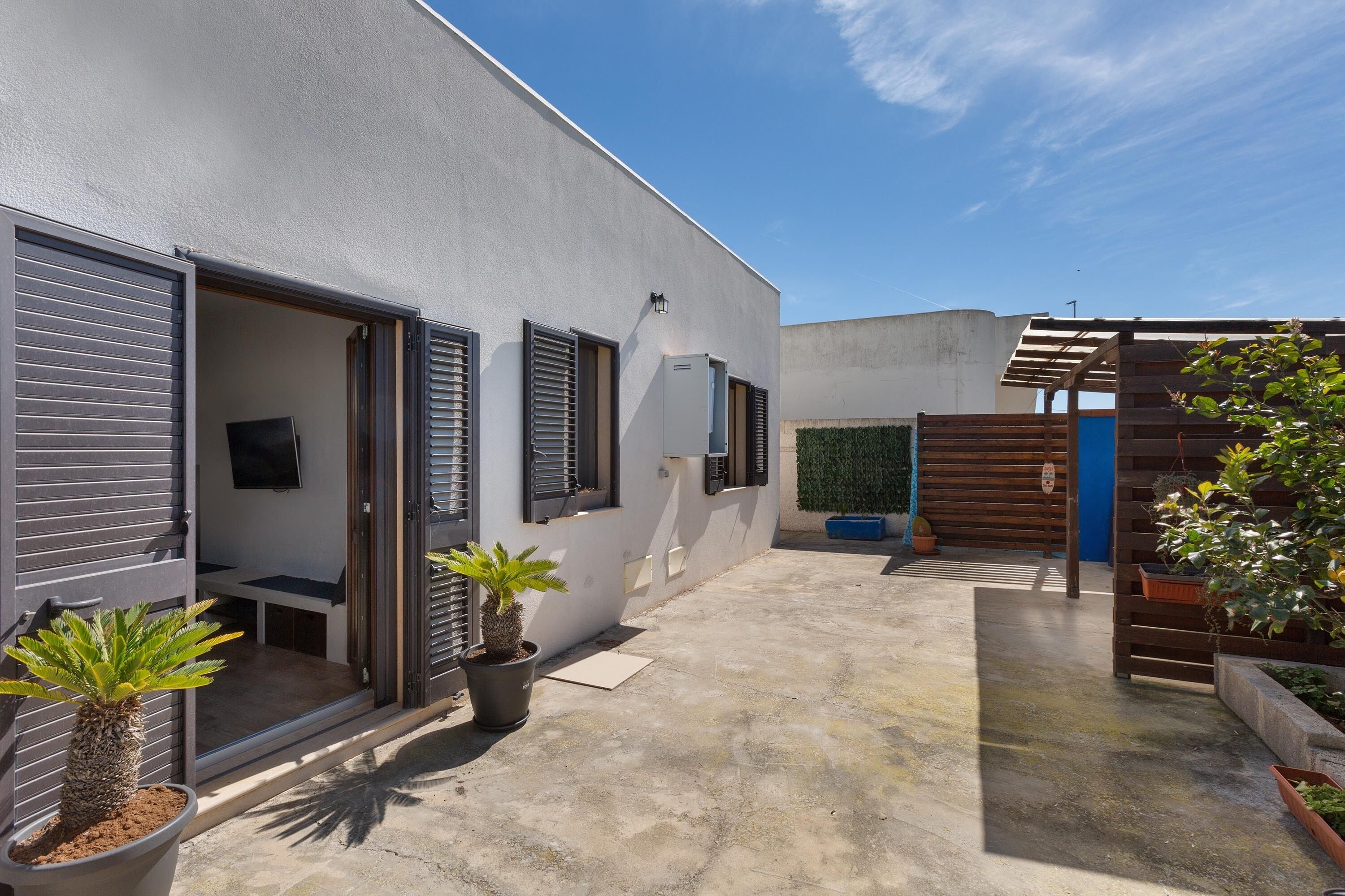 A modern building with a flat roof, a small patio area with potted plants, and a wooden pergola.