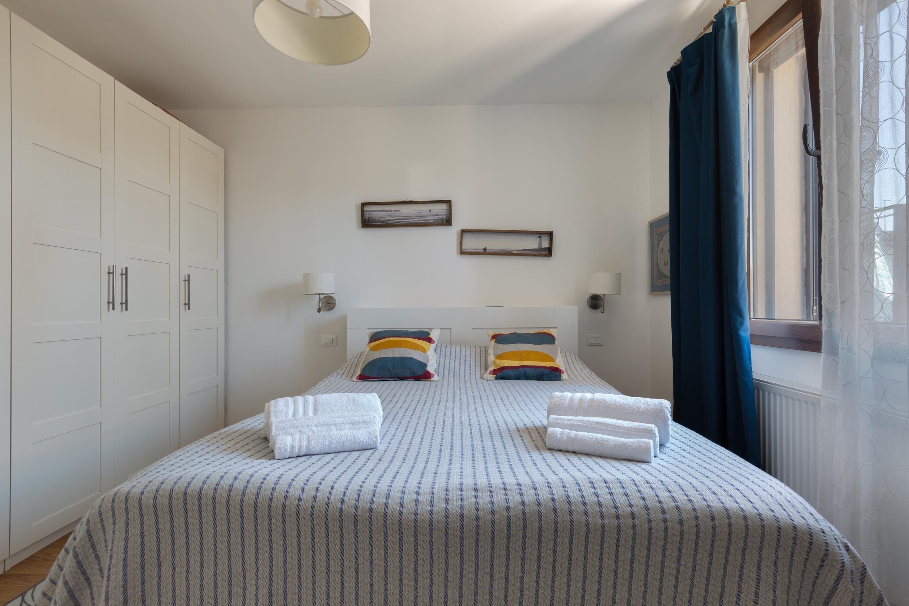 A bedroom with a large bed, two bedside tables, a wardrobe, and a window with curtains.