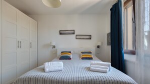 Une chambre à coucher avec un grand lit, deux tables de chevet, une armoire et une fenêtre avec des rideaux.