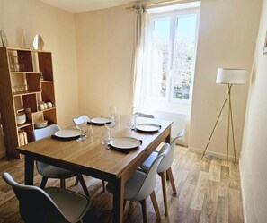 A dining area with a wooden table set for four, surrounded by chairs. A bookshelf with various items is to the left. - Apartment - shaded terrace (Marsanne)