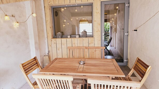 A wooden interior with a table and chairs, a large window, and string lights. - Apartment - shaded terrace (Marsanne)