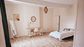A room with a bed, a desk with a chair, a standing mirror, a wall-mounted lamp, and a door. - Apartment - shaded terrace (Marsanne)