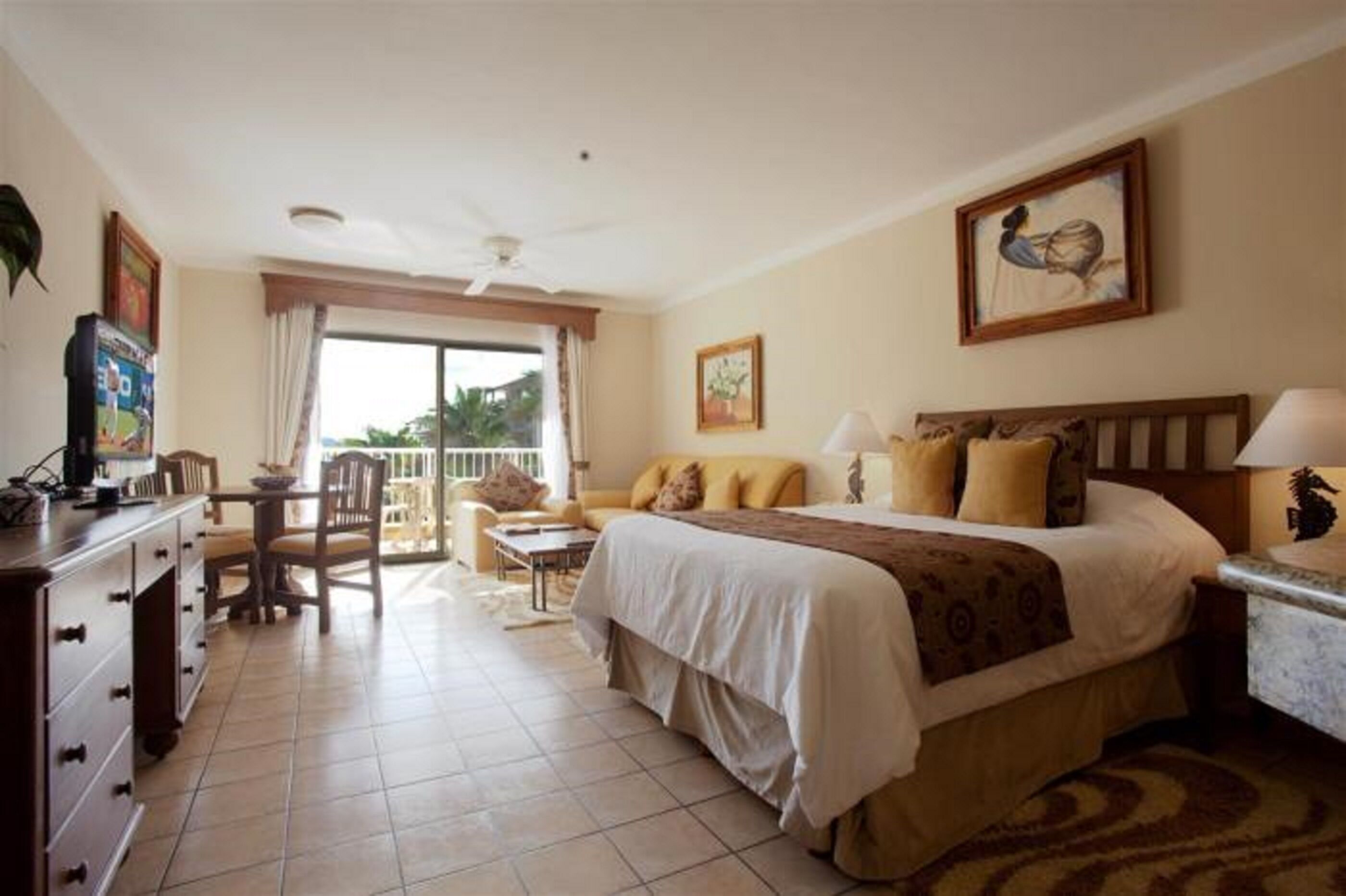 A hotel room with a bed, a desk, a chair, a dining table, and a balcony with a view.