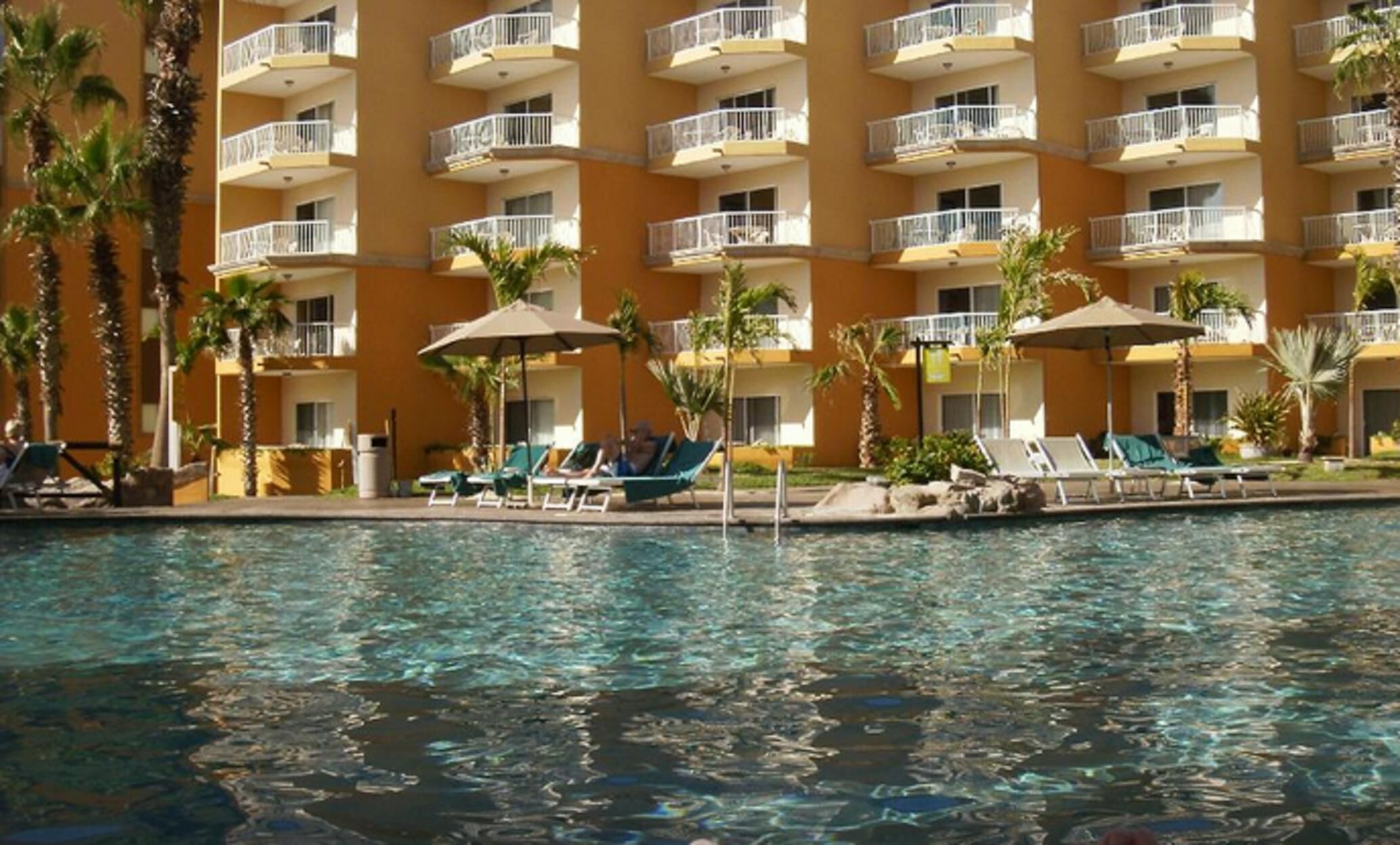 A hotel with a pool area, including lounge chairs and umbrellas, surrounded by palm trees.