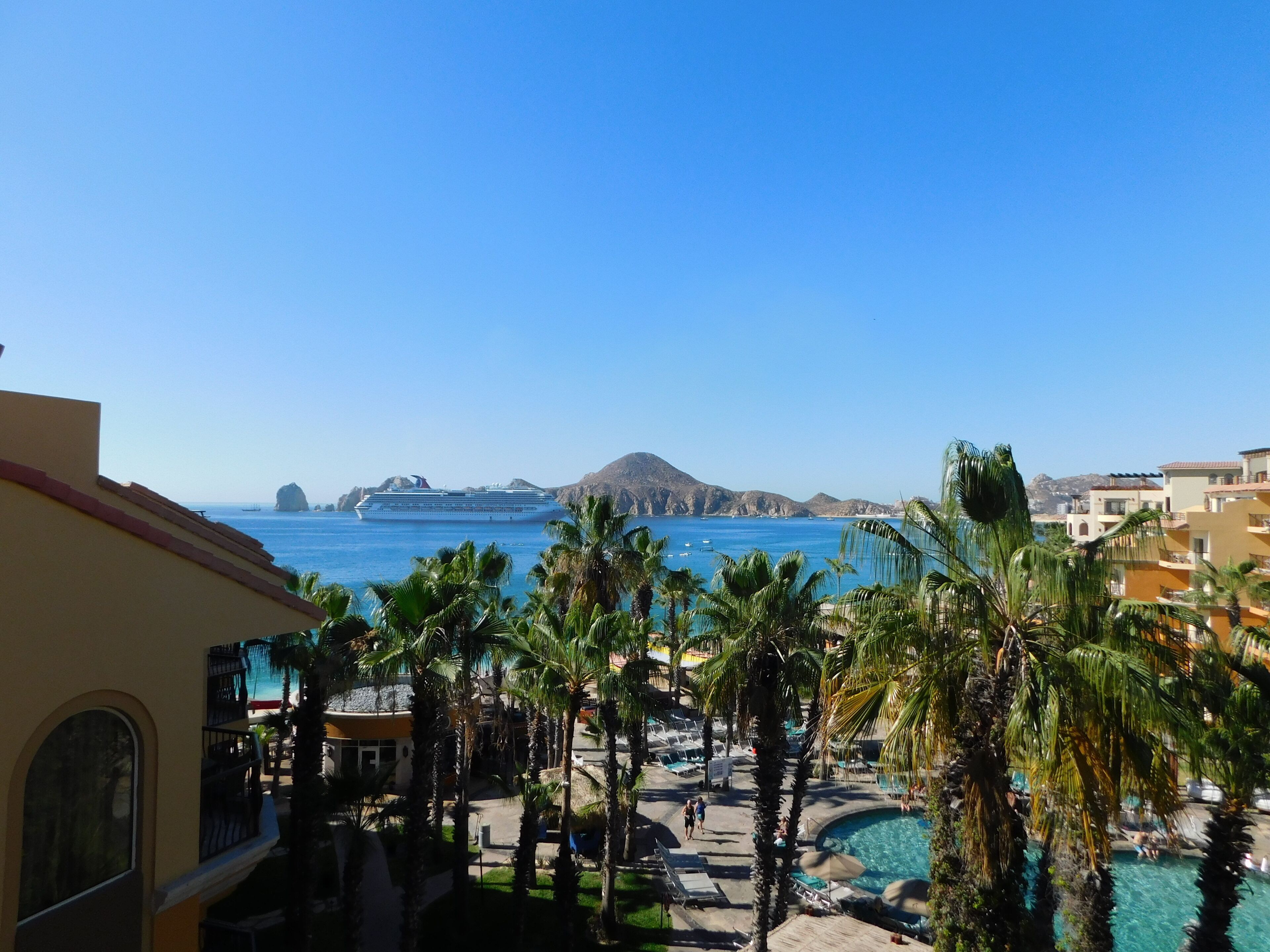 Un resort con piscina, palme e vista sul mare e sulle montagne.