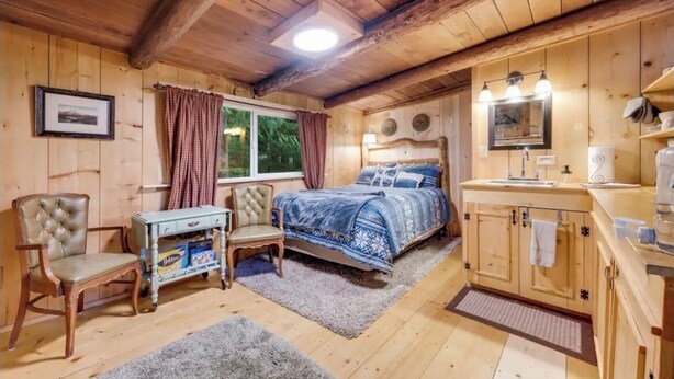 Acogedora habitación tipo cabaña con cama, una silla, una mesita y una ventana con cortinas.